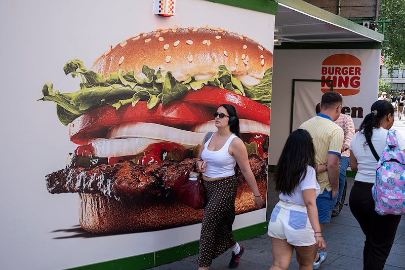 Los visitantes de Leicester Square observan una valla publicitaria a gran escala que cubre el restaurante Burger King. Los visitantes de Leicester Square observan una valla publicitaria a gran escala que cubre el restaurante Burger King.