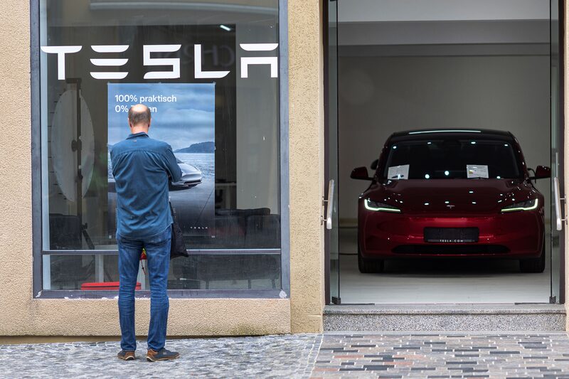 Homem parado em frente a uma concessionária Tesla. Ele observa um carro exposto na vitrine Homem parado em frente a uma concessionária Tesla. Ele observa um carro exposto na vitrine