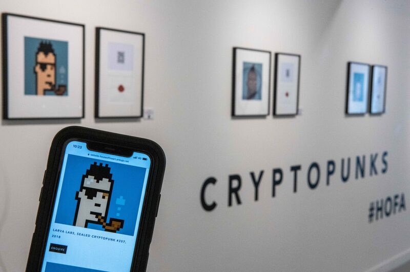 Un asistente de la galería sostiene un teléfono inteligente que muestra la litografía firmada "Sealed Cryptopunk # 207" de Larva Labs. Un asistente de la galería sostiene un teléfono inteligente que muestra la litografía firmada "Sealed Cryptopunk # 207" de Larva Labs.