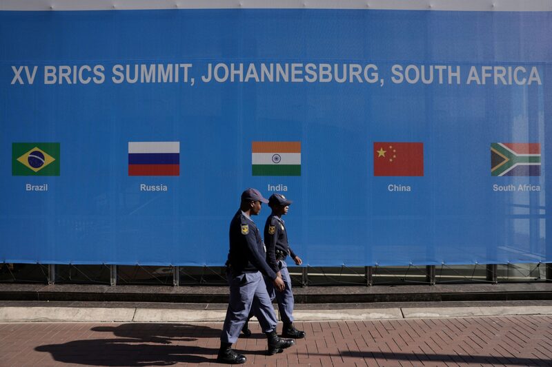 South African police officers walk in front of an event banner outside the venue for the BRICS summit at the Sandton Convention Center in the Sandton district of Johannesburg, South Africa, on Monday, Aug. 21, 2023. The summit of BRICS leaders is scheduled to take place from Aug. 22-24 in Johannesburg, where they will discuss whether to admit more nations to its ranks. South African police officers walk in front of an event banner outside the venue for the BRICS summit at the Sandton Convention Center in the Sandton district of Johannesburg, South Africa, on Monday, Aug. 21, 2023. The summit of BRICS leaders is scheduled to take place from Aug. 22-24 in Johannesburg, where they will discuss whether to admit more nations to its ranks.