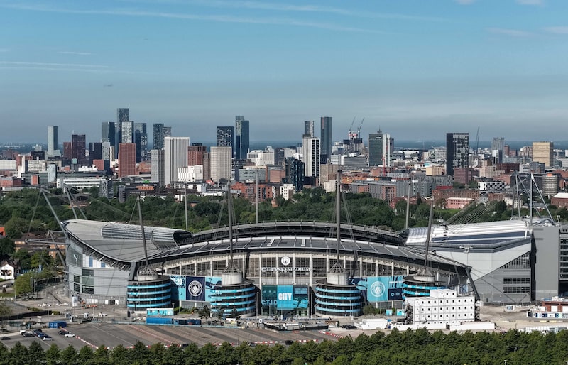 Vista panorámica del Etihad Stadium, sede del Manchester City, con el horizonte urbano de Manchester al fondo. Vista panorámica del Etihad Stadium, sede del Manchester City, con el horizonte urbano de Manchester al fondo.