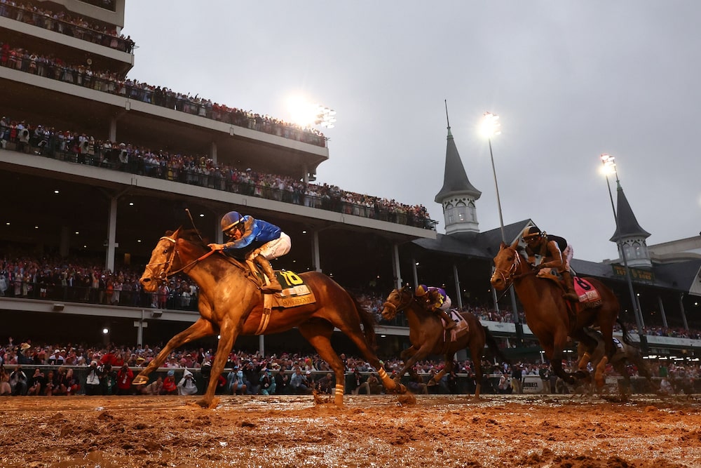 Caballos compiten en el Kentucky Derby mientras el público sigue la carrera desde las tribunas del hipódromo Churchill Downs. Caballos compiten en el Kentucky Derby mientras el público sigue la carrera desde las tribunas del hipódromo Churchill Downs.