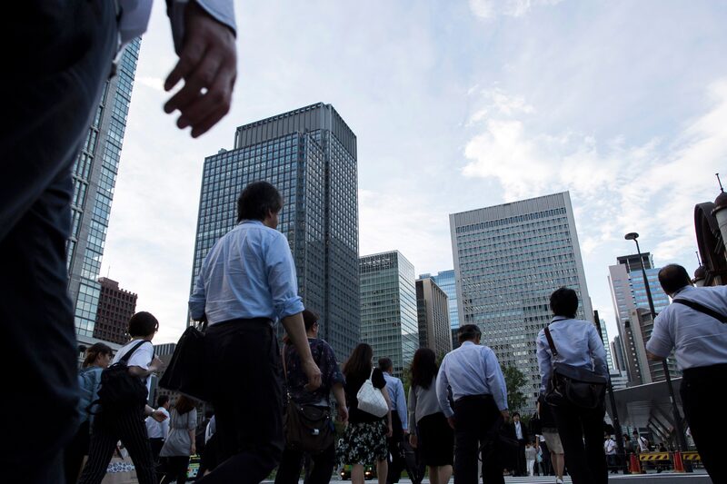 Los viajeros caminan frente a edificios comerciales en Tokio, Japón. Los viajeros caminan frente a edificios comerciales en Tokio, Japón.
