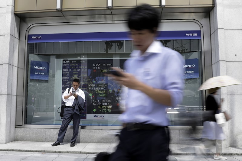Un peatón que utiliza su teléfono inteligente se encuentra frente a un tablero electrónico de valores fuera de una firma de valores en Tokio, Japón, el jueves 30 de agosto de 2018. Fotógrafo: Kiyoshi Ota/Bloomberg Un peatón que utiliza su teléfono inteligente se encuentra frente a un tablero electrónico de valores fuera de una firma de valores en Tokio, Japón, el jueves 30 de agosto de 2018. Fotógrafo: Kiyoshi Ota/Bloomberg