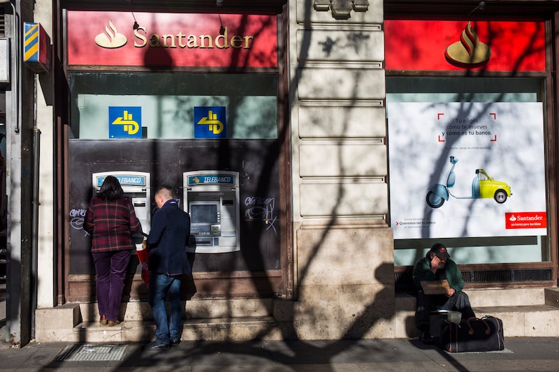 Un hombre sostiene un cartel pidiendo contribuciones a los transeúntes mientras está sentado junto a los cajeros automáticos (ATM) fuera de una sucursal del Banco Santander SA en Madrid, España, el viernes 9 de enero de 2015. La decisión de Ana Botín de recaudar 7500 millones de euros (8900 millones de dólares) en nuevos fondos para el Banco Santander SA ha indignado a algunos inversores que añoran los días en que su padre dirigía el banco. Un hombre sostiene un cartel pidiendo contribuciones a los transeúntes mientras está sentado junto a los cajeros automáticos (ATM) fuera de una sucursal del Banco Santander SA en Madrid, España, el viernes 9 de enero de 2015. La decisión de Ana Botín de recaudar 7500 millones de euros (8900 millones de dólares) en nuevos fondos para el Banco Santander SA ha indignado a algunos inversores que añoran los días en que su padre dirigía el banco.