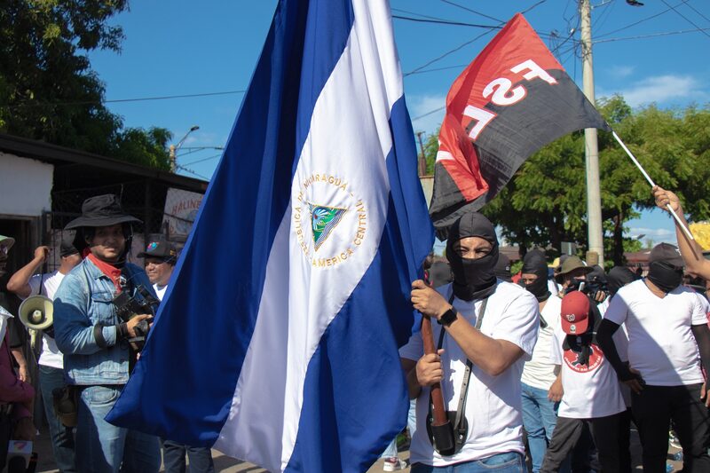 En primer plano, un civil encapuchado juramentado como "policía voluntario" por el gobierno de Daniel Ortega y Rosario Murillo, durante la denominada Caminata de la Revolución: ¡Paz, Unidad y Victoria!, el 1 de abril. En primer plano, un civil encapuchado juramentado como "policía voluntario" por el gobierno de Daniel Ortega y Rosario Murillo, durante la denominada Caminata de la Revolución: ¡Paz, Unidad y Victoria!, el 1 de abril.