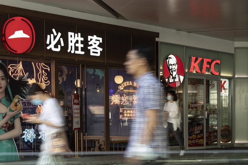 Pessoas passando em frente a uma unidade da Pizza Hut e uma unidade do KFC Pessoas passando em frente a uma unidade da Pizza Hut e uma unidade do KFC