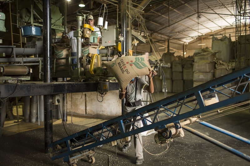 Un trabajador transporta un saco de arpillera con granos de café arábica en la zona de empaquetado de una planta en Machado, estado de Minas Gerais, Brasil. Fotógrafo: Rodrigo Capote/Bloomberg. Un trabajador transporta un saco de arpillera con granos de café arábica en la zona de empaquetado de una planta en Machado, estado de Minas Gerais, Brasil. Fotógrafo: Rodrigo Capote/Bloomberg.