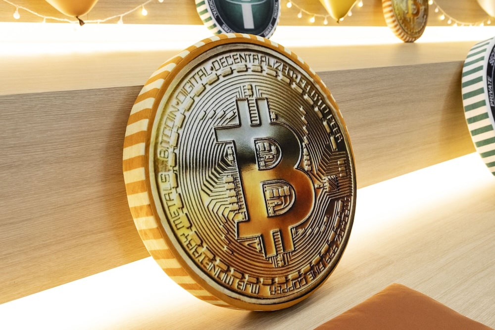 El logotipo de Bitcoin en un cojín expuesto en una oficina de intercambio de Bithumb en Seúl, Corea del Sur. El logotipo de Bitcoin en un cojín expuesto en una oficina de intercambio de Bithumb en Seúl, Corea del Sur.