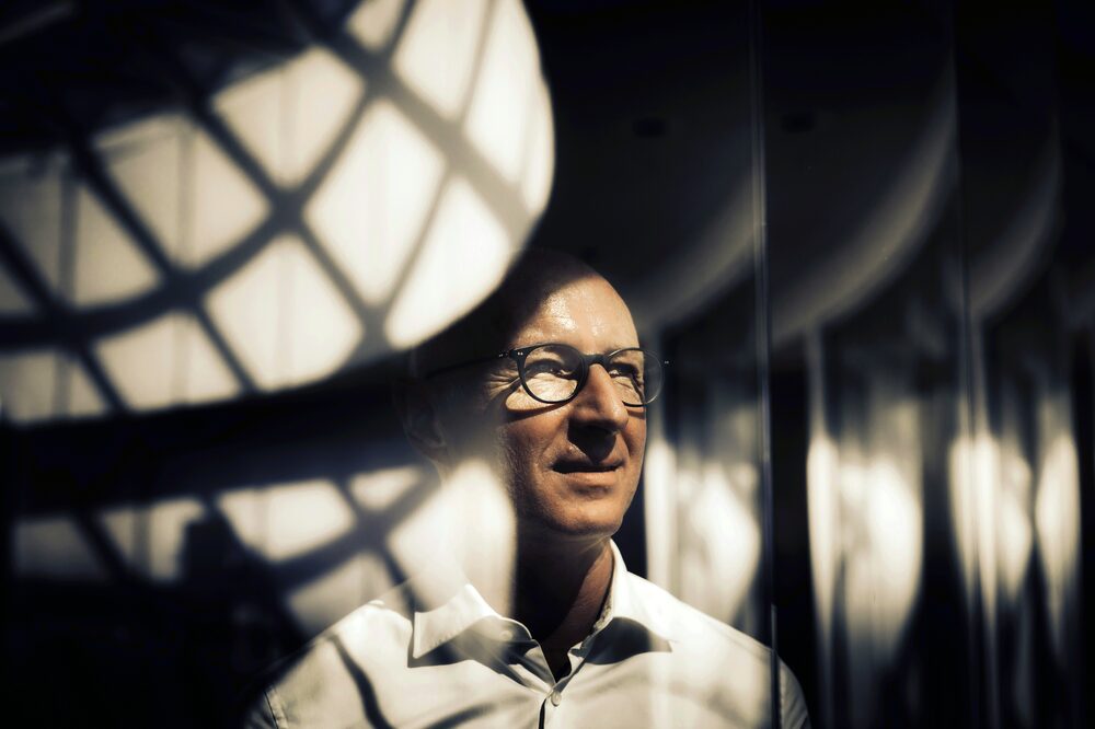 Homem visto através de um vidro, os reflexos ficam na frente de seu rosto mas é possível ver algumas feições Homem visto através de um vidro, os reflexos ficam na frente de seu rosto mas é possível ver algumas feições