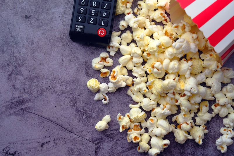 Un control remoto y un recipiente de palomitas de maíz, símbolos del consumo de contenido audiovisual en plataformas de streaming. Un control remoto y un recipiente de palomitas de maíz, símbolos del consumo de contenido audiovisual en plataformas de streaming.