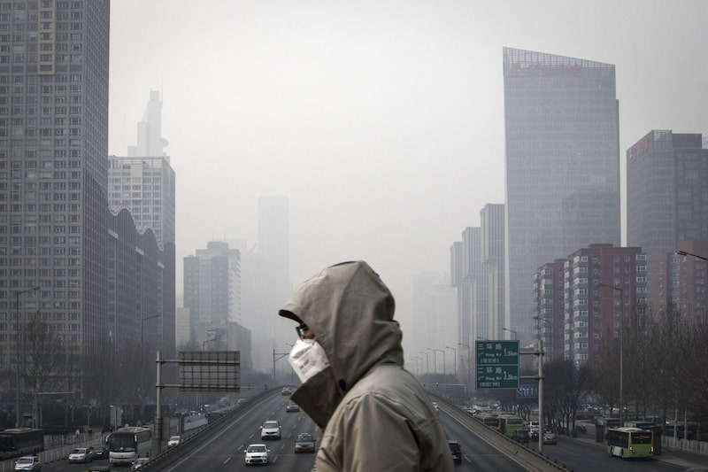 A man wearing a face mask walks on a footbridge as buildings shrouded in haze stands in the background in Beijing. A man wearing a face mask walks on a footbridge as buildings shrouded in haze stands in the background in Beijing.