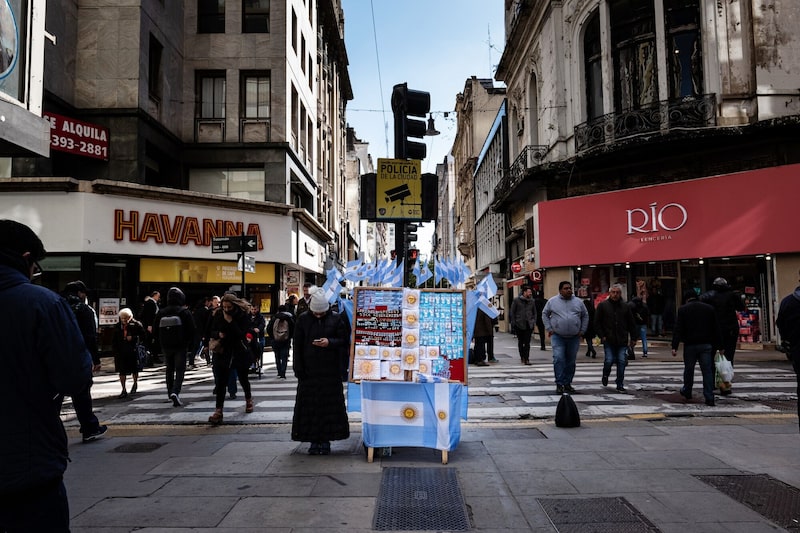 Los peatones pasan junto a un vendedor de recuerdos de la bandera argentina en la calle en Buenos Aires, Argentina. Los peatones pasan junto a un vendedor de recuerdos de la bandera argentina en la calle en Buenos Aires, Argentina.
