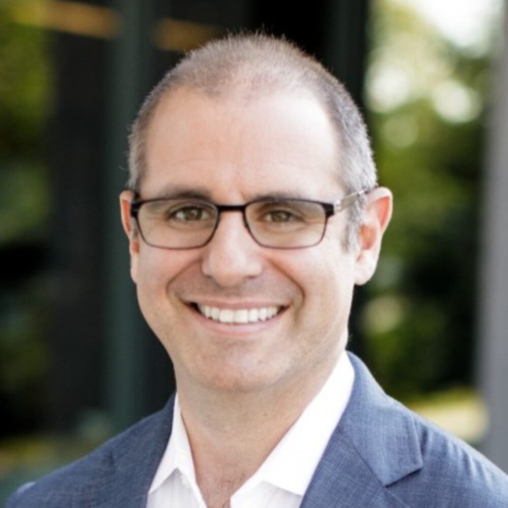 Foto do busto de um homem de óculos, cabelos calvos e grisalhos que sorri para a câmera Foto do busto de um homem de óculos, cabelos calvos e grisalhos que sorri para a câmera