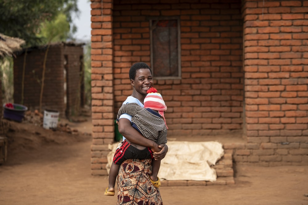 Meria Tambala e seu filho de dois anos, Chikondi, do lado de fora de sua casa. Ela em breve será conectada à rede elétrica Meria Tambala e seu filho de dois anos, Chikondi, do lado de fora de sua casa. Ela em breve será conectada à rede elétrica