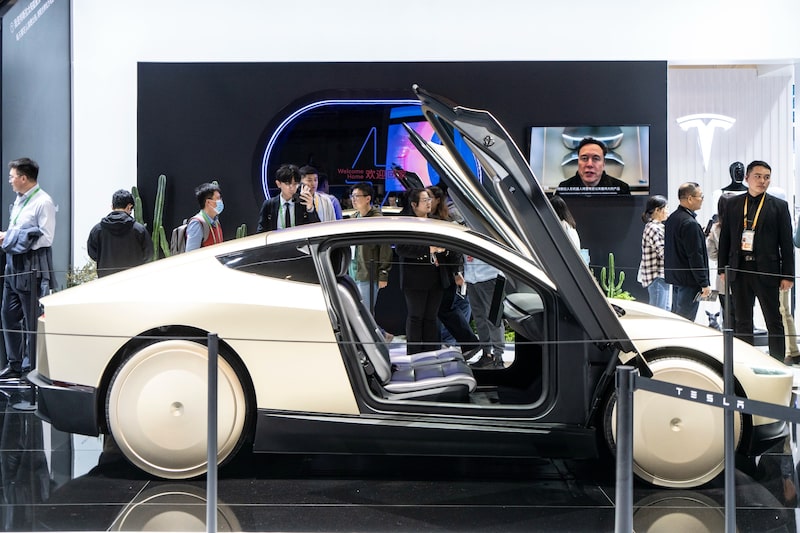 Visitantes observan un prototipo de vehículo eléctrico en el stand de Tesla durante una feria tecnológica. En pantalla, el CEO Elon Musk aparece en una transmisión. Visitantes observan un prototipo de vehículo eléctrico en el stand de Tesla durante una feria tecnológica. En pantalla, el CEO Elon Musk aparece en una transmisión.