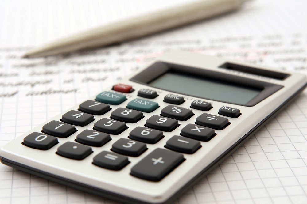 Una imagen de una calculadora acompaña de unas cuentas en un papel. Una imagen de una calculadora acompaña de unas cuentas en un papel.