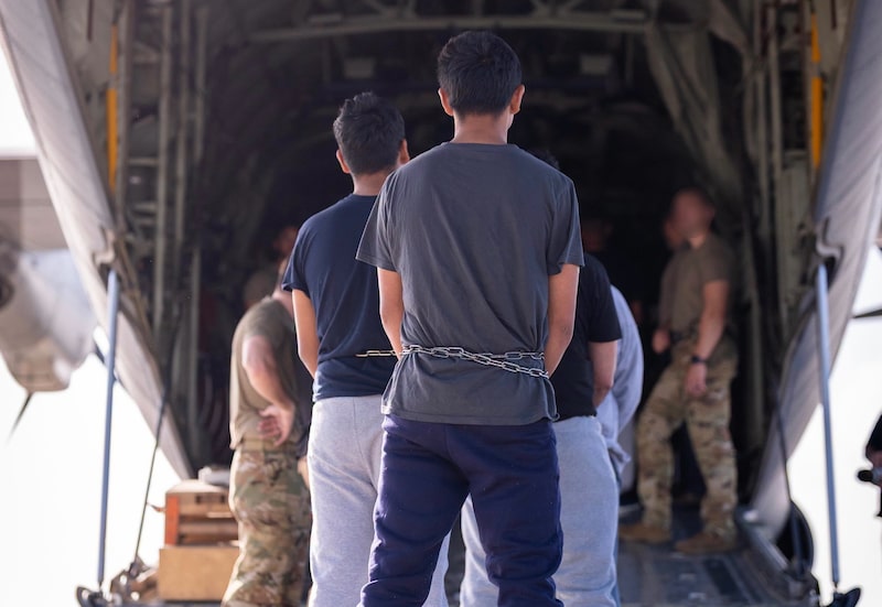 Personas esposadas son trasladadas frente a la rampa de un avión de transporte militar estadounidense durante un operativo de deportación. Personas esposadas son trasladadas frente a la rampa de un avión de transporte militar estadounidense durante un operativo de deportación.
