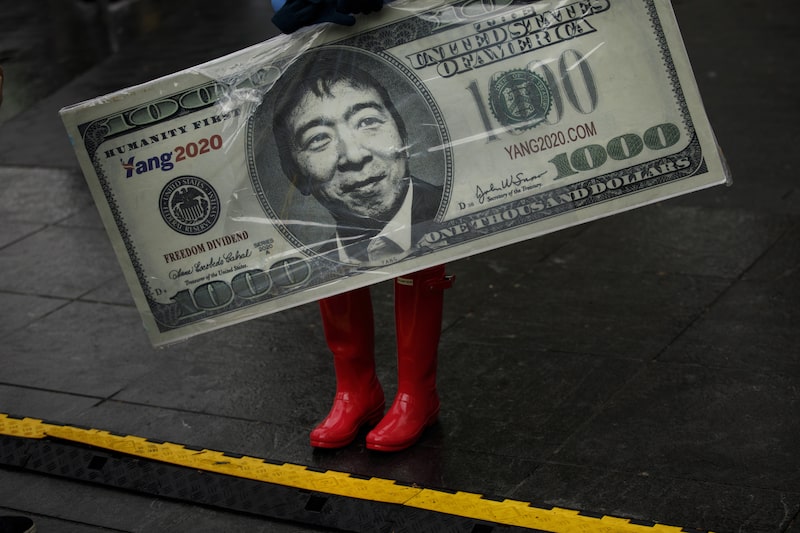 Placa faz referência à proposta de renda básica universal de US$ 1.000 por mês de Andrew Yang durante ato na Washington Square Park, em Nova York, em maio de 2019. Placa faz referência à proposta de renda básica universal de US$ 1.000 por mês de Andrew Yang durante ato na Washington Square Park, em Nova York, em maio de 2019.