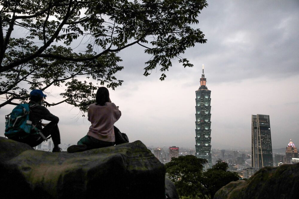Personas sobre una roca mientras observan cómo edificios se iluminan al anochecer en Taipei. Personas sobre una roca mientras observan cómo edificios se iluminan al anochecer en Taipei.