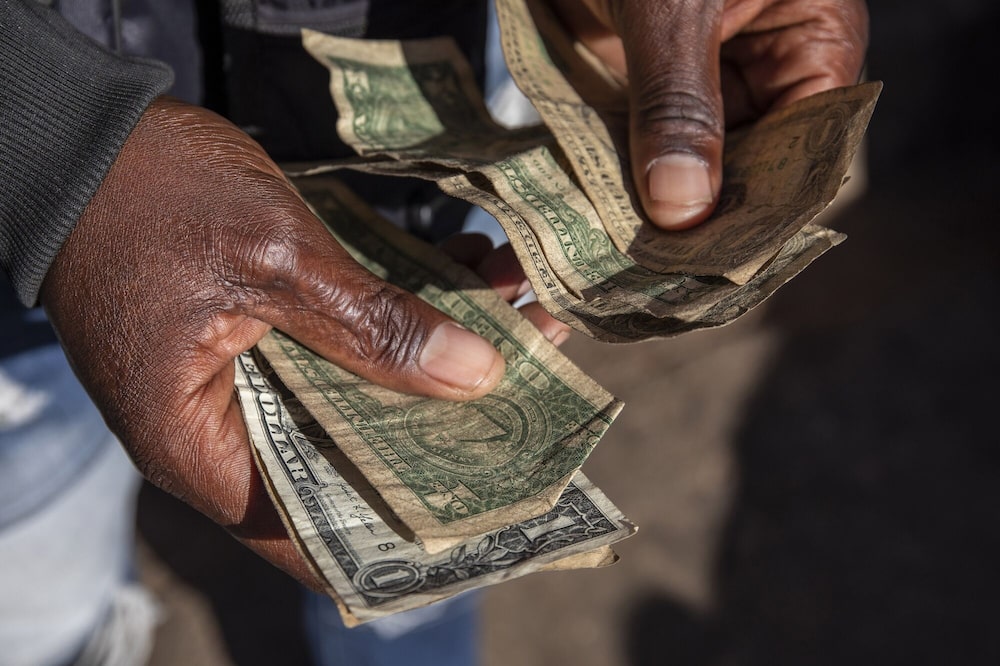 Un operador informal de cambio de divisas cuenta billetes de un dólar estadounidense en el distrito financiero central de Harare, Zimbabue. Un operador informal de cambio de divisas cuenta billetes de un dólar estadounidense en el distrito financiero central de Harare, Zimbabue.