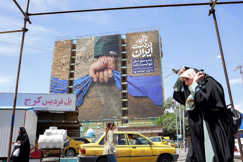 A woman adjusts her headdress as she walks near a billboard on the facade of a building depicting the Strait of Hormuz with a caption in Persian reading "Forever in Iran's Hand", at Vanak Square in Tehran on May 6, 2026. The United States and Pakistan, a key mediator in the Middle East war, expressed new hope of talks leading to a peace deal with Iran on May 6, after President Donald Trump halted a plan to guide ships through the Strait of Hormuz. (Photo by AFP via Getty Images) / A woman adjusts her headdress as she walks near a billboard on the facade of a building depicting the Strait of Hormuz with a caption in Persian reading "Forever in Iran's Hand", at Vanak Square in Tehran on May 6, 2026. The United States and Pakistan, a key mediator in the Middle East war, expressed new hope of talks leading to a peace deal with Iran on May 6, after President Donald Trump halted a plan to guide ships through the Strait of Hormuz. (Photo by AFP via Getty Images) /