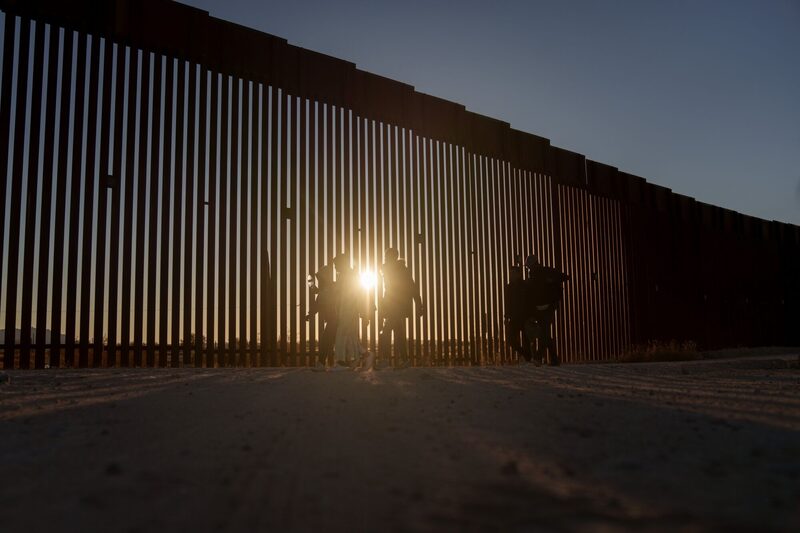 Migrantes caminan junto a la valla fronteriza entre Estados Unidos y México en Lukeville, Arizona, EE. UU., el martes 12 de diciembre de 2023. La afluencia de migrantes que cruzan ilegalmente la frontera en la remota localidad de Lukeville, Arizona, ha desbordado a los funcionarios fronterizos estadounidenses, lo que les ha llevado a cerrar el puerto de entrada oficial para destinar recursos al procesamiento de las llegadas ilegales. Migrantes caminan junto a la valla fronteriza entre Estados Unidos y México en Lukeville, Arizona, EE. UU., el martes 12 de diciembre de 2023. La afluencia de migrantes que cruzan ilegalmente la frontera en la remota localidad de Lukeville, Arizona, ha desbordado a los funcionarios fronterizos estadounidenses, lo que les ha llevado a cerrar el puerto de entrada oficial para destinar recursos al procesamiento de las llegadas ilegales.