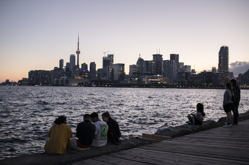 People sit on a dock along the skyline during sunset in Toronto, Ontario, Canada People sit on a dock along the skyline during sunset in Toronto, Ontario, Canada