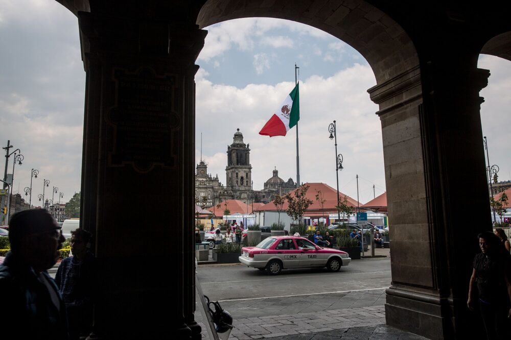Un taxi pasa frente a la bandera mexicana que ondea en la Plaza de la Constitución (Zócalo) en la Ciudad de México. Un taxi pasa frente a la bandera mexicana que ondea en la Plaza de la Constitución (Zócalo) en la Ciudad de México.