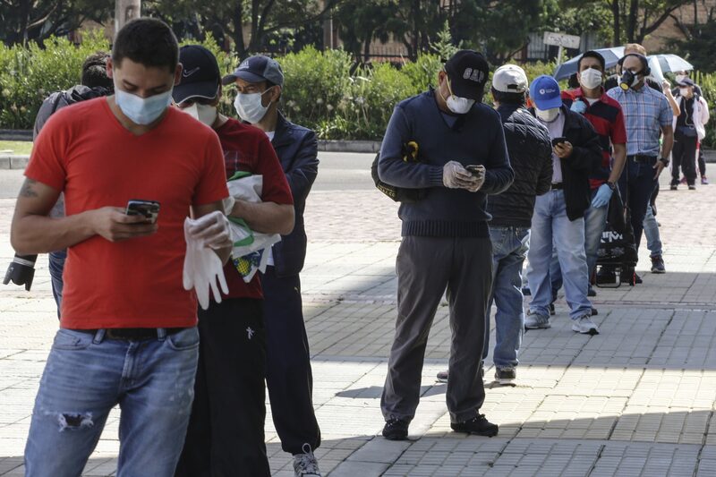 Hombres con máscaras protectoras hacen fila, mientras practican el distanciamiento social, frente a un centro comercial en Bogotá, Colombia, el lunes 13 de abril de 2020. Hombres con máscaras protectoras hacen fila, mientras practican el distanciamiento social, frente a un centro comercial en Bogotá, Colombia, el lunes 13 de abril de 2020.