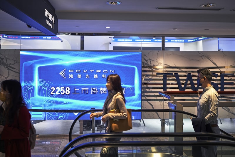 Un grupo de personas pasa junto a un cartel que anuncia la salida a bolsa de Foxtron Vehicle Technologies Co. en la Bolsa de Taiwán. Un grupo de personas pasa junto a un cartel que anuncia la salida a bolsa de Foxtron Vehicle Technologies Co. en la Bolsa de Taiwán.