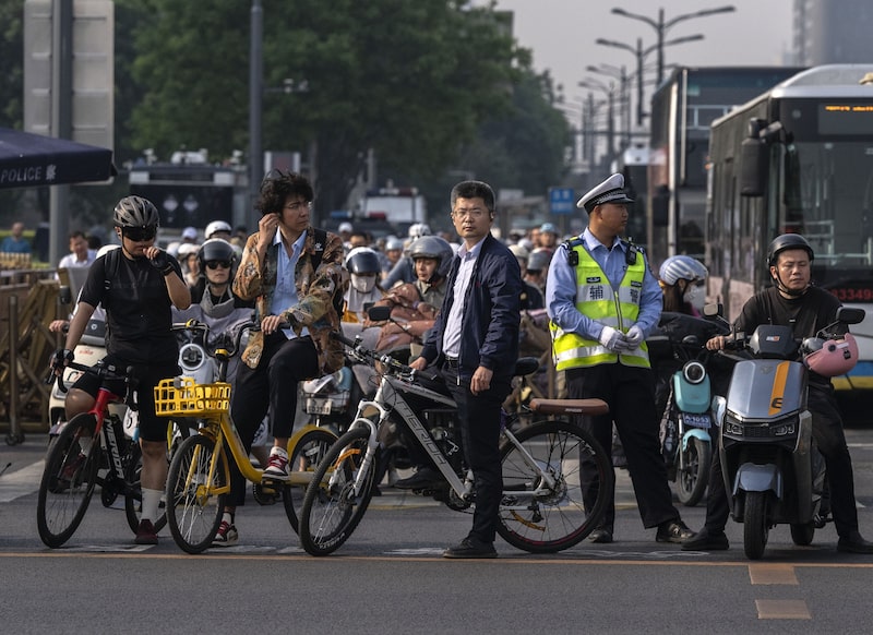 Unos viajeros esperan en un semáforo junto a un agente de policía cerca de la plaza de Tiananmen. Fotógrafo: Kevin Frayer/Getty Images Unos viajeros esperan en un semáforo junto a un agente de policía cerca de la plaza de Tiananmen. Fotógrafo: Kevin Frayer/Getty Images