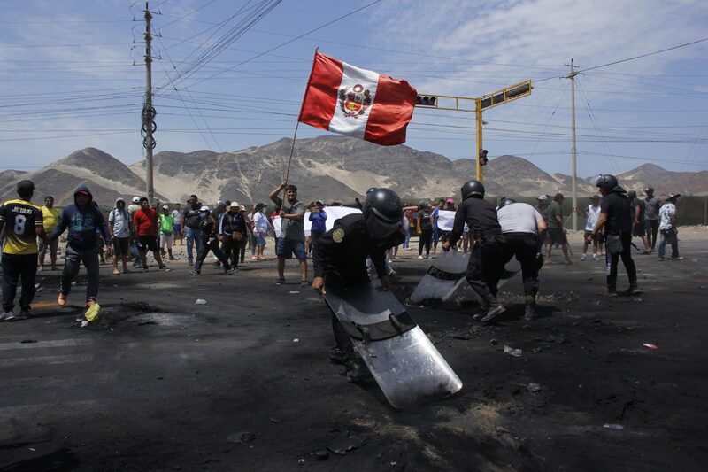 Agentes de la policía antidisturbios barren los escombros mientras un manifestante agita una bandera nacional peruana en la carretera Panamericana Norte durante las protestas en Trujillo, Perú, el jueves 15 de diciembre de 2022. Perú ha declarado el estado de emergencia en todo el país, suspendiendo los derechos básicos durante 30 días, para tratar de restablecer el orden en medio de disturbios violentos generalizados. Fotógrafo: Arturo Gutarra Chavez/Bloomberg Agentes de la policía antidisturbios barren los escombros mientras un manifestante agita una bandera nacional peruana en la carretera Panamericana Norte durante las protestas en Trujillo, Perú, el jueves 15 de diciembre de 2022. Perú ha declarado el estado de emergencia en todo el país, suspendiendo los derechos básicos durante 30 días, para tratar de restablecer el orden en medio de disturbios violentos generalizados. Fotógrafo: Arturo Gutarra Chavez/Bloomberg