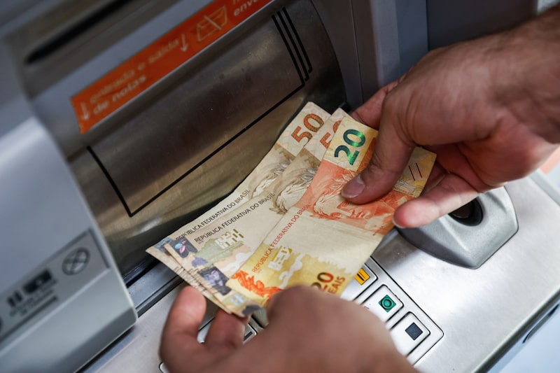 Un cliente retira billetes de reales brasileños. Fotógrafo: Tuane Fernandes/Bloomberg. Un cliente retira billetes de reales brasileños. Fotógrafo: Tuane Fernandes/Bloomberg.