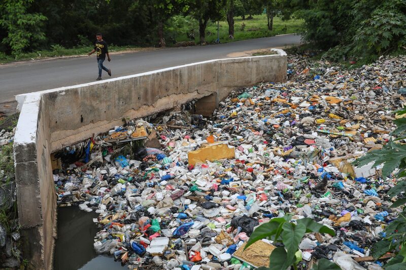 Un peatón camina por un puente sobre una alcantarilla, bloqueada por residuos de plástico y basura, en Accra, Ghana, el lunes 4 de julio de 2022. Un peatón camina por un puente sobre una alcantarilla, bloqueada por residuos de plástico y basura, en Accra, Ghana, el lunes 4 de julio de 2022.