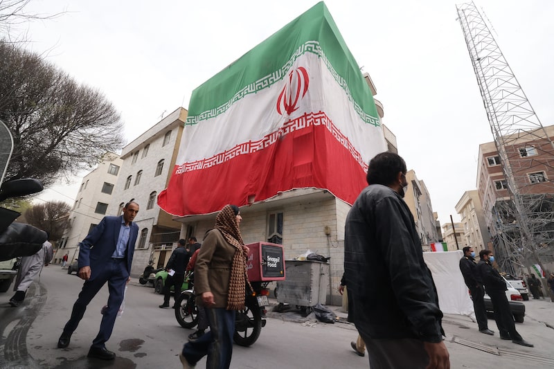 Una enorme bandera iraní adorna un edificio mientras los iraníes caminan junto a estructuras dañadas tras un ataque militar anterior en la capital iraní, Teherán, el 15 de marzo de 2026. Una enorme bandera iraní adorna un edificio mientras los iraníes caminan junto a estructuras dañadas tras un ataque militar anterior en la capital iraní, Teherán, el 15 de marzo de 2026.