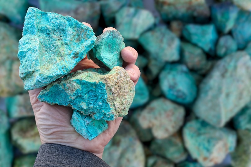 Mineral de óxido de cobre (Cu) verde azul, sostenido en la mano, contra el fondo de mineral que está fuera de foco. Minería Mineral de óxido de cobre (Cu) verde azul, sostenido en la mano, contra el fondo de mineral que está fuera de foco. Minería
