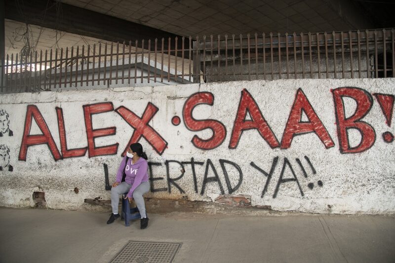 A pedestrian wearing a protective mask sits near a wall with graffiti that reads in Spanish "Free Alex Saab Now!" in the Petare neighborhood of Caracas, Venezuela, on Thursday, Feb. 4, 2021. President Nicolas Maduro's Colombian financier Alex Saab is being labeled "the peoples savior" in new graffiti across Caracas ahead of a key hearing Friday on his alleged role in bribing Venezuelan officials. Photographer: Carlos Becerra/Bloomberg A pedestrian wearing a protective mask sits near a wall with graffiti that reads in Spanish "Free Alex Saab Now!" in the Petare neighborhood of Caracas, Venezuela, on Thursday, Feb. 4, 2021. President Nicolas Maduro's Colombian financier Alex Saab is being labeled "the peoples savior" in new graffiti across Caracas ahead of a key hearing Friday on his alleged role in bribing Venezuelan officials. Photographer: Carlos Becerra/Bloomberg