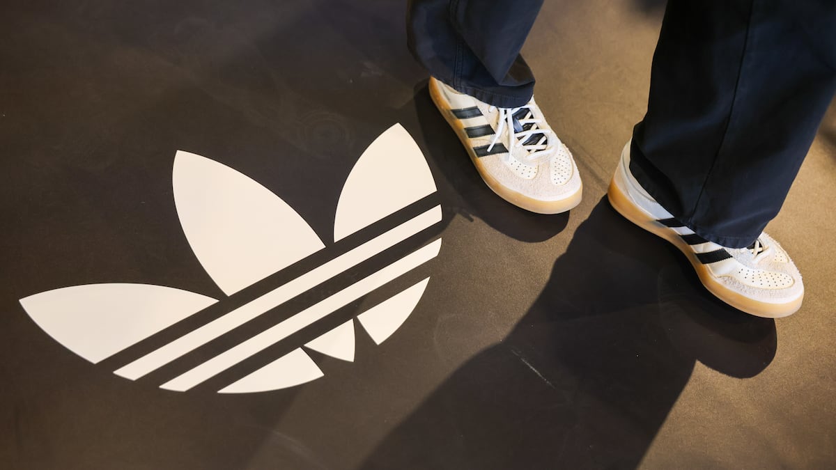 Una mujer que lleva zapatillas de la colaboración entre Bad Bunny y Adidas AG camina cerca de un logotipo en la tienda insignia de la marca en Herzogenaurach, Alemania.