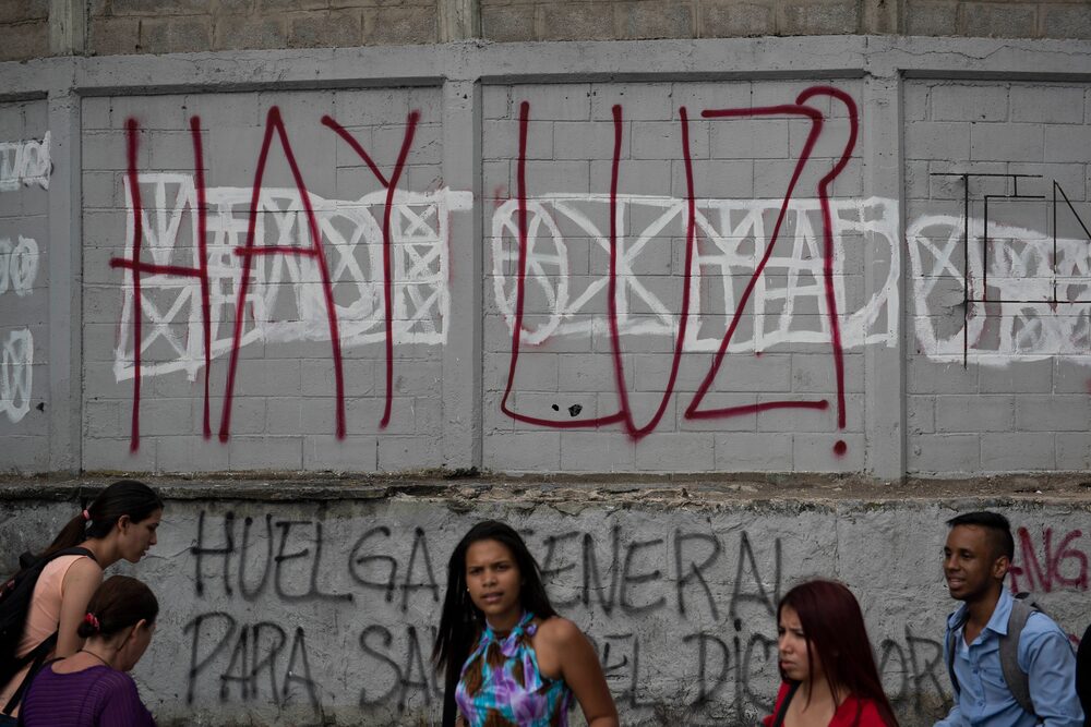Peatones pasan frente a un graffiti que dice "¿Tienes Luces?" en el barrio Chacaito de Caracas. 25 de marzo de 2019. Peatones pasan frente a un graffiti que dice "¿Tienes Luces?" en el barrio Chacaito de Caracas. 25 de marzo de 2019.