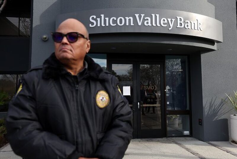 Un guardia de seguridad del Silicon Valley Bank vigila una fila de personas fuera de la oficina el 13 de marzo de 2023 en Santa Clara, California. Un guardia de seguridad del Silicon Valley Bank vigila una fila de personas fuera de la oficina el 13 de marzo de 2023 en Santa Clara, California.