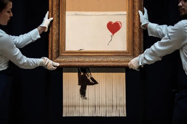 Empleados de Sotheby's posan con 'Love is in the Bin', del artista británico Banksy.dfd