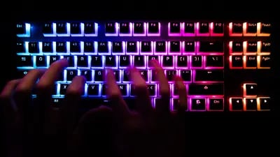 Un hombre escribiendo en un teclado de computadora retroiluminado.