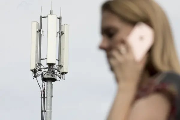 Un peatón utiliza un teléfono móvil a la vista de las antenas de un mástil de telecomunicaciones de telefonía móvil en esta fotografía arreglada en Shalford, Reino Unido, el lunes 13 de julio de 2020.