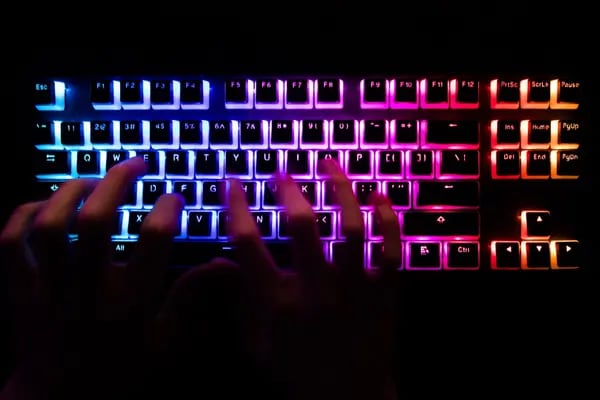 Un hombre escribiendo en un teclado de ordenador iluminado.