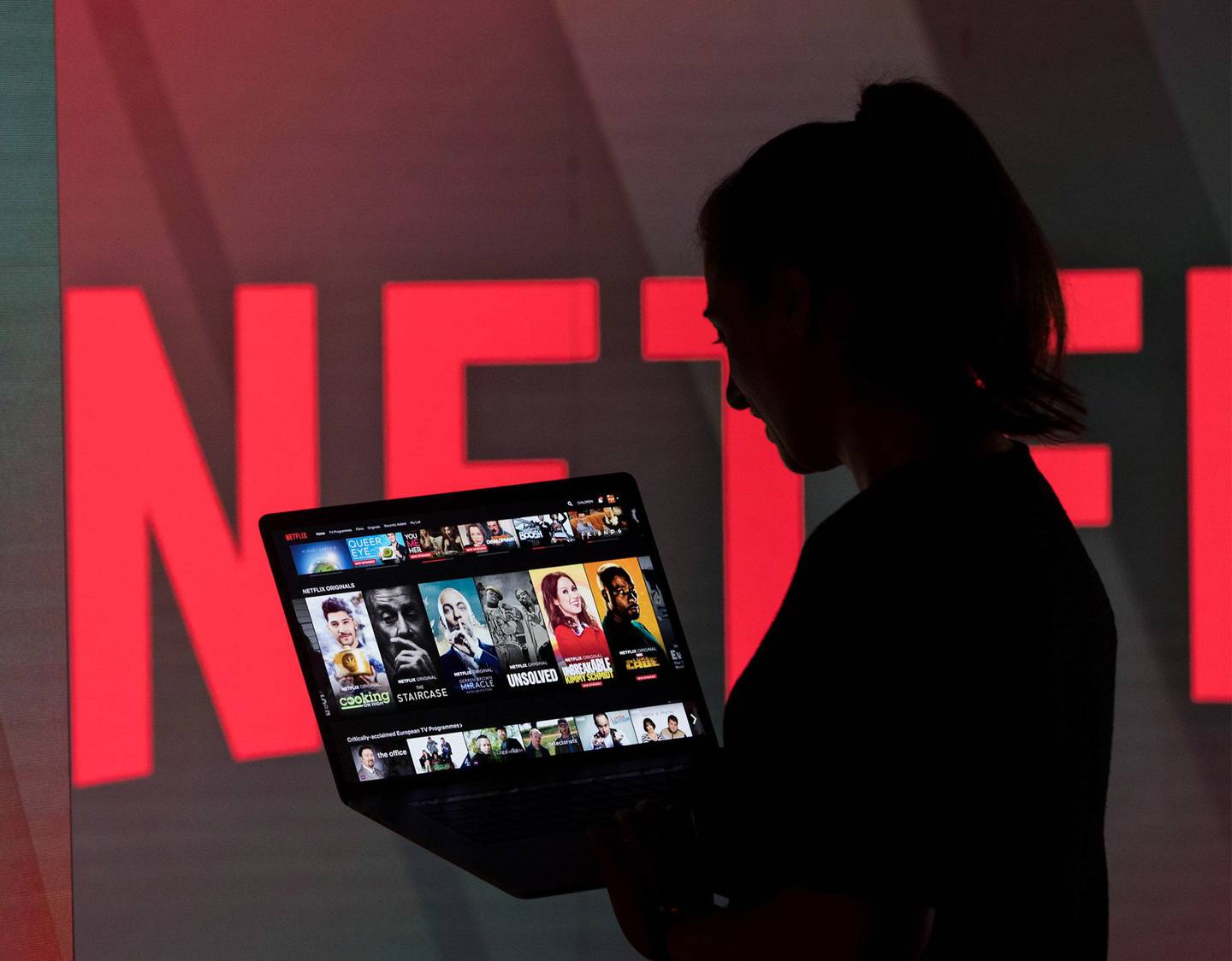 A woman browses the Netflix Inc. homepage on a laptop computer amongst illuminated screens bearing the company logo in this arranged photograph in London, U.K.